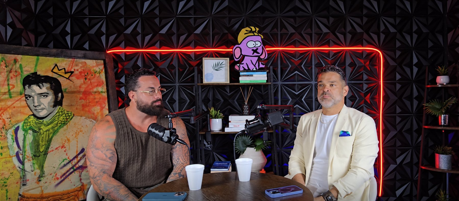 Two speakers in The HUB Voices podcast studio with red accent lighting.