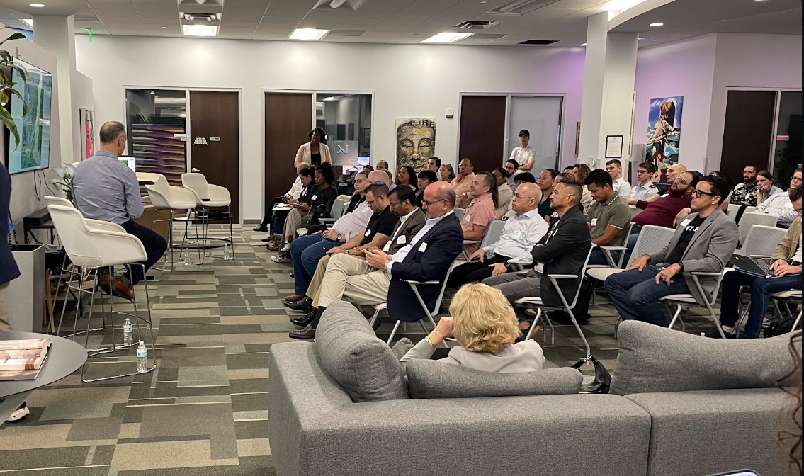 A packed community event in The HUB lounge, with members and guests listening to a speaker